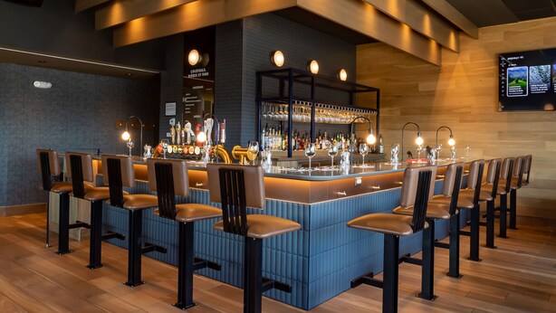 A bar area with a long counter, multiple stools, and a modern ceiling design. - Rodeway Inn (Gaspé)