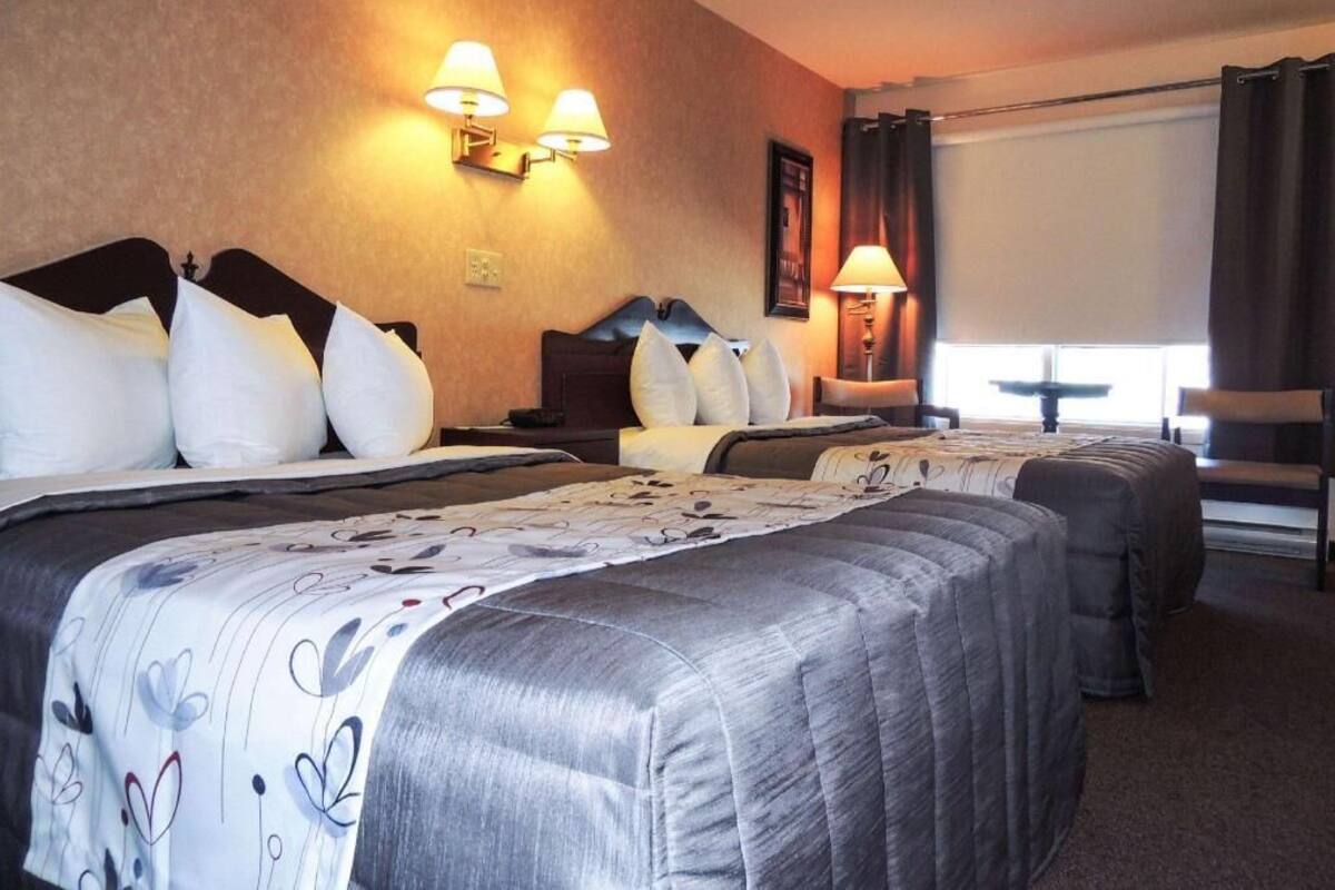 A hotel room with two beds, a desk, a chair, and a window with curtains.