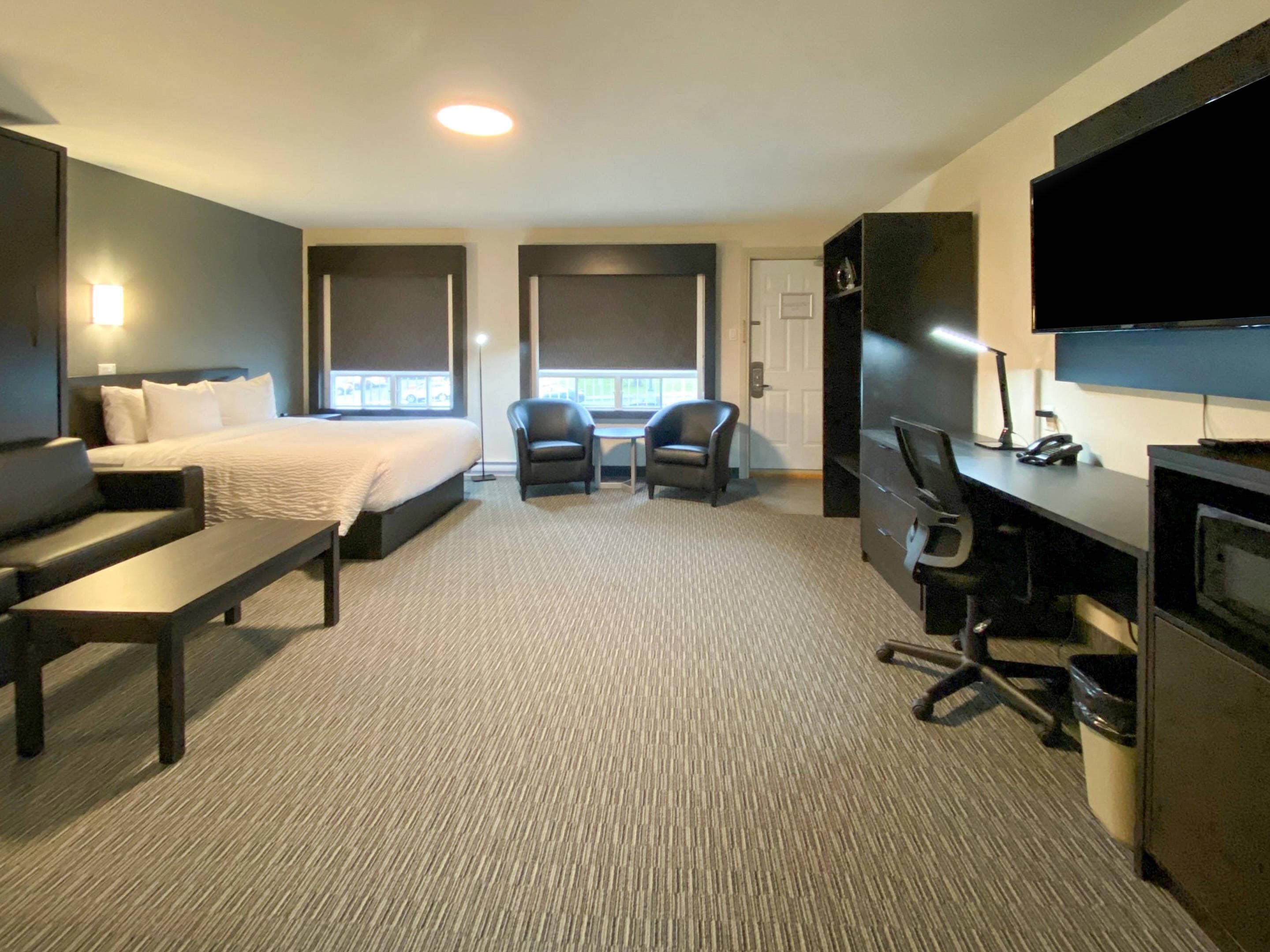A hotel room with a bed, two chairs, a desk, a TV, and a large window.