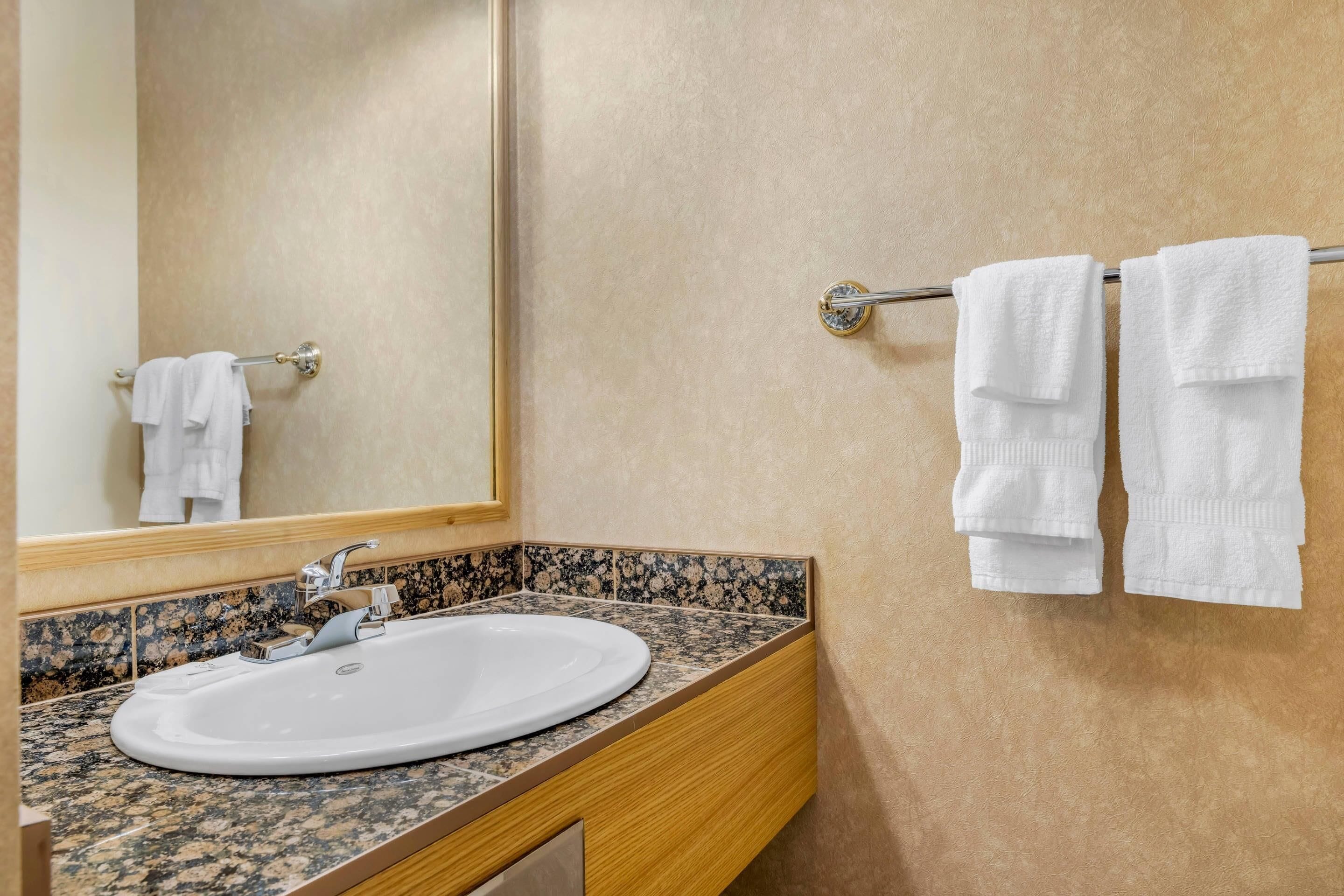 Un baño con lavamanos, espejo y toallero.