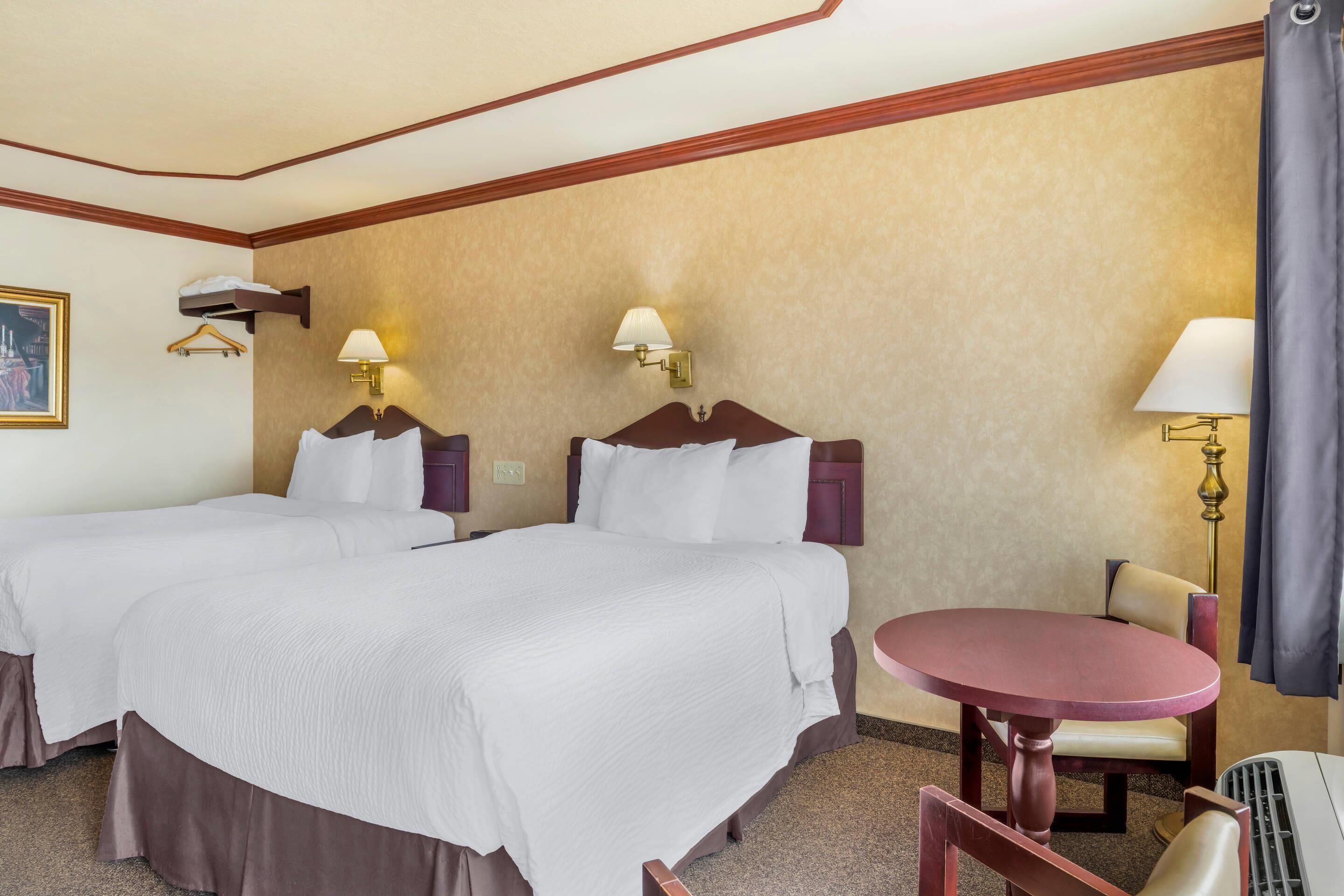 A hotel room with two beds, a round table, and a chair.
