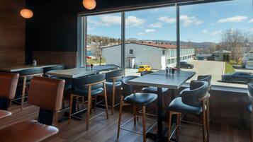A modern restaurant with large windows, wooden flooring, and black bar stools.