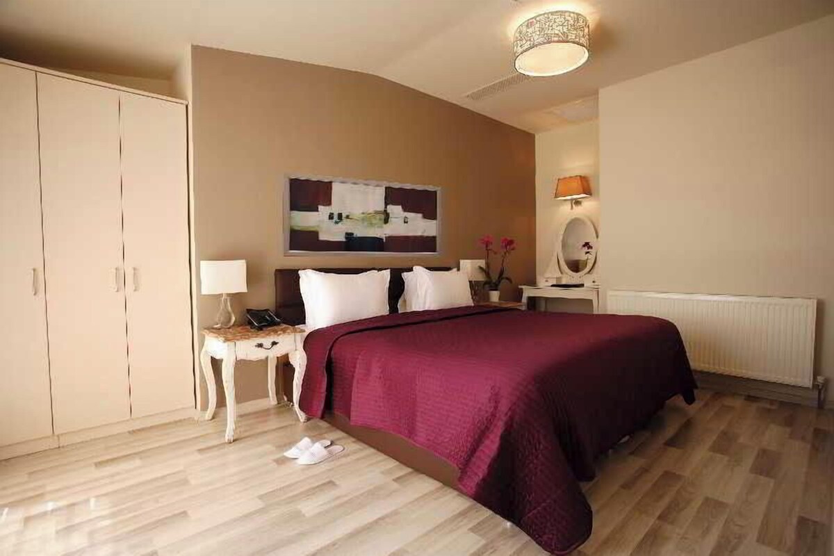 A hotel room with a large bed, a bedside table with a lamp, a dresser, and a painting on the wall.