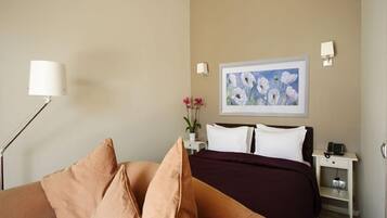 A hotel room with a bed, a nightstand, a lamp, a painting, and a sofa.