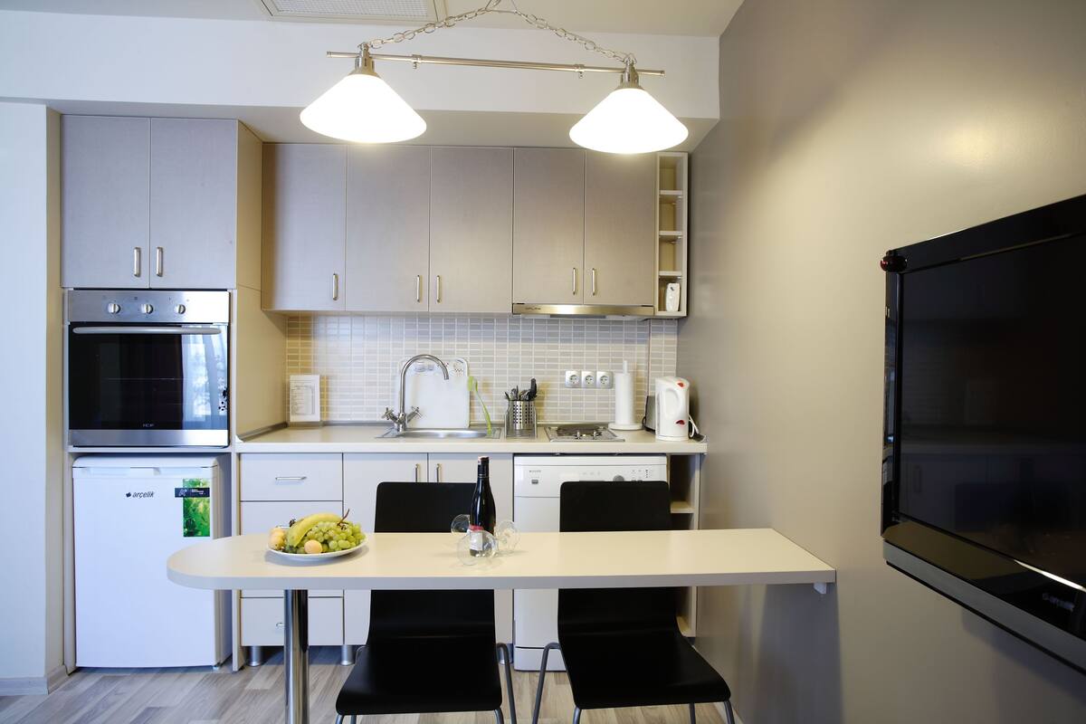 A modern kitchen with stainless steel appliances, a white countertop, and black chairs around a table.