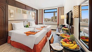 Een hotelkamer met twee bedden, een eettafel met fruit, een televisie en uitzicht over de stad.