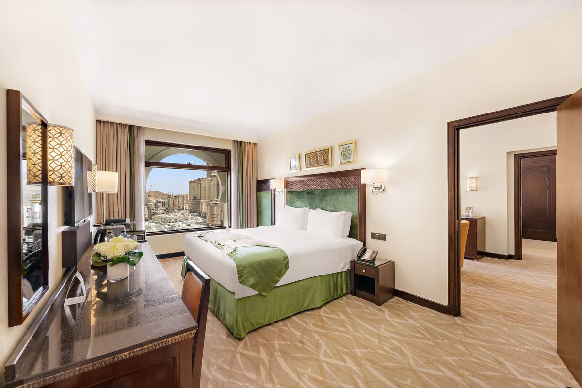 A hotel room with a large bed, a desk with a lamp, a view of the city, and a mirror.