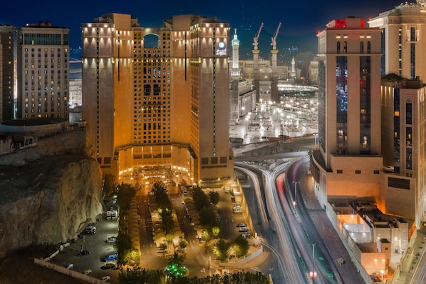 A nighttime cityscape with illuminated buildings, a busy highway, and a large mosque with minarets.
