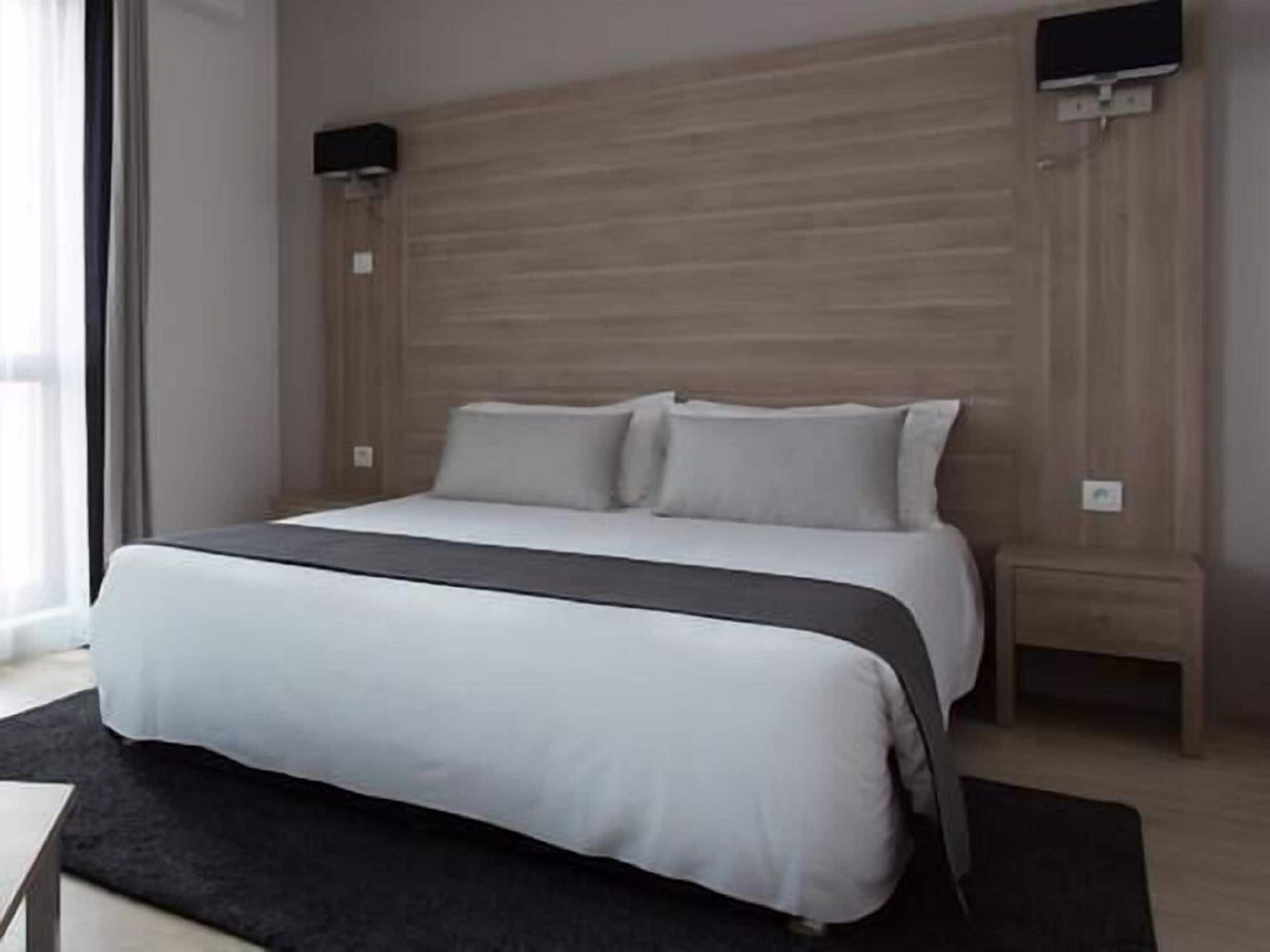 A modern hotel room with a large bed, a bedside table, and a flat-screen TV mounted on the wall.