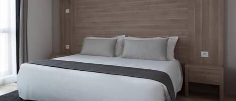 Una habitación de hotel moderna con una cama grande, una mesita de noche y un televisor de pantalla plana montado en la pared.