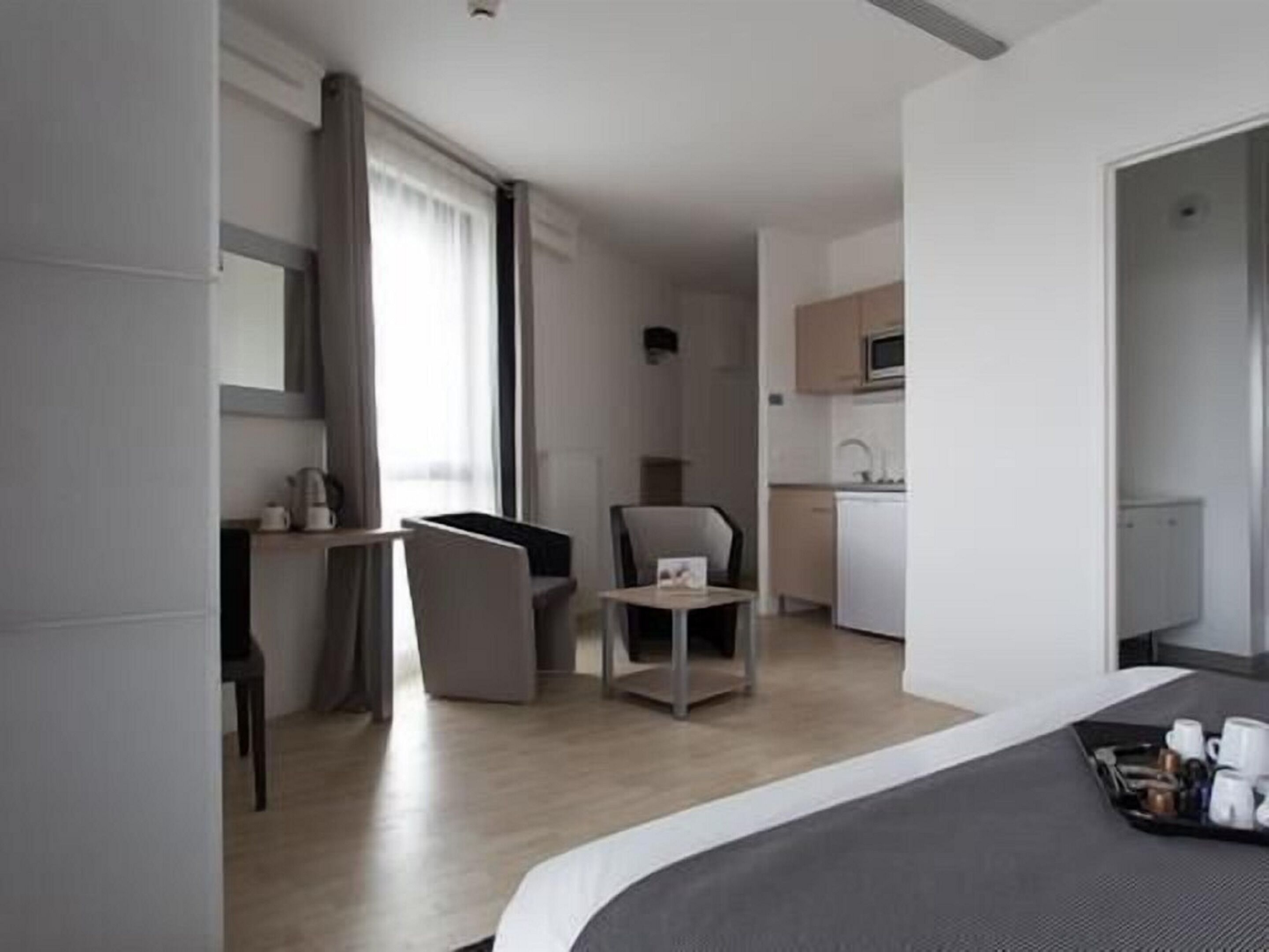 A modern hotel room with a bed, a desk, a chair, and a kitchenette.