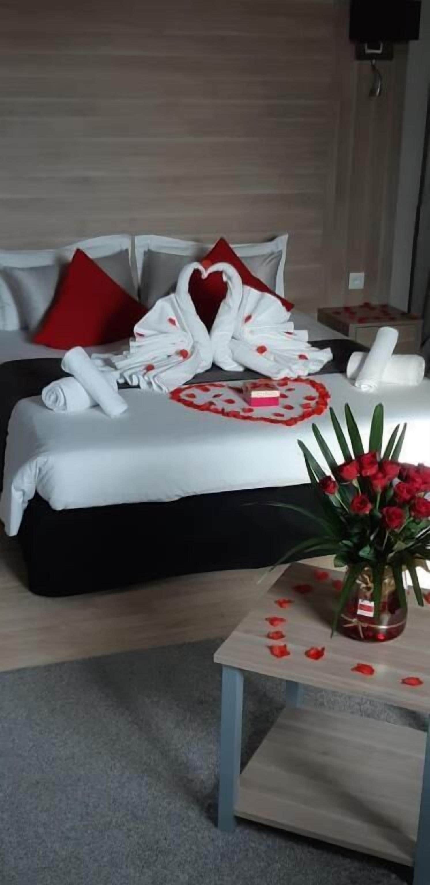 Una habitación de hotel con una cama bien hecha, un jarrón de rosas rojas y una mesita con un jarrón.