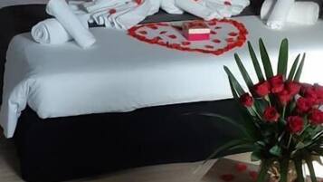 Una habitación de hotel con una cama bien hecha, un jarrón de rosas rojas y una mesita con un jarrón.