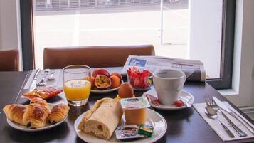 Ein Esstisch mit Croissants, Eiern und Orangensaft, vor einem Fenster mit Blick auf ein Gebäude.