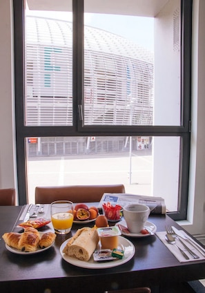 A breakfast table with croissants, eggs, and orange juice, set in front of a window with a view of a building. - Twenty Business Flats Lille Grand Stade (Villeneuve-d'Ascq)