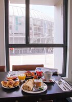 Una mesa de desayuno con croissants, huevos y jugo de naranja, frente a una ventana con vista a un edificio.