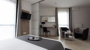 Ett modernt hotellrum med en stor säng, ett skrivbord, en stol, en tv och ett litet bord med ett bricka med koppar.