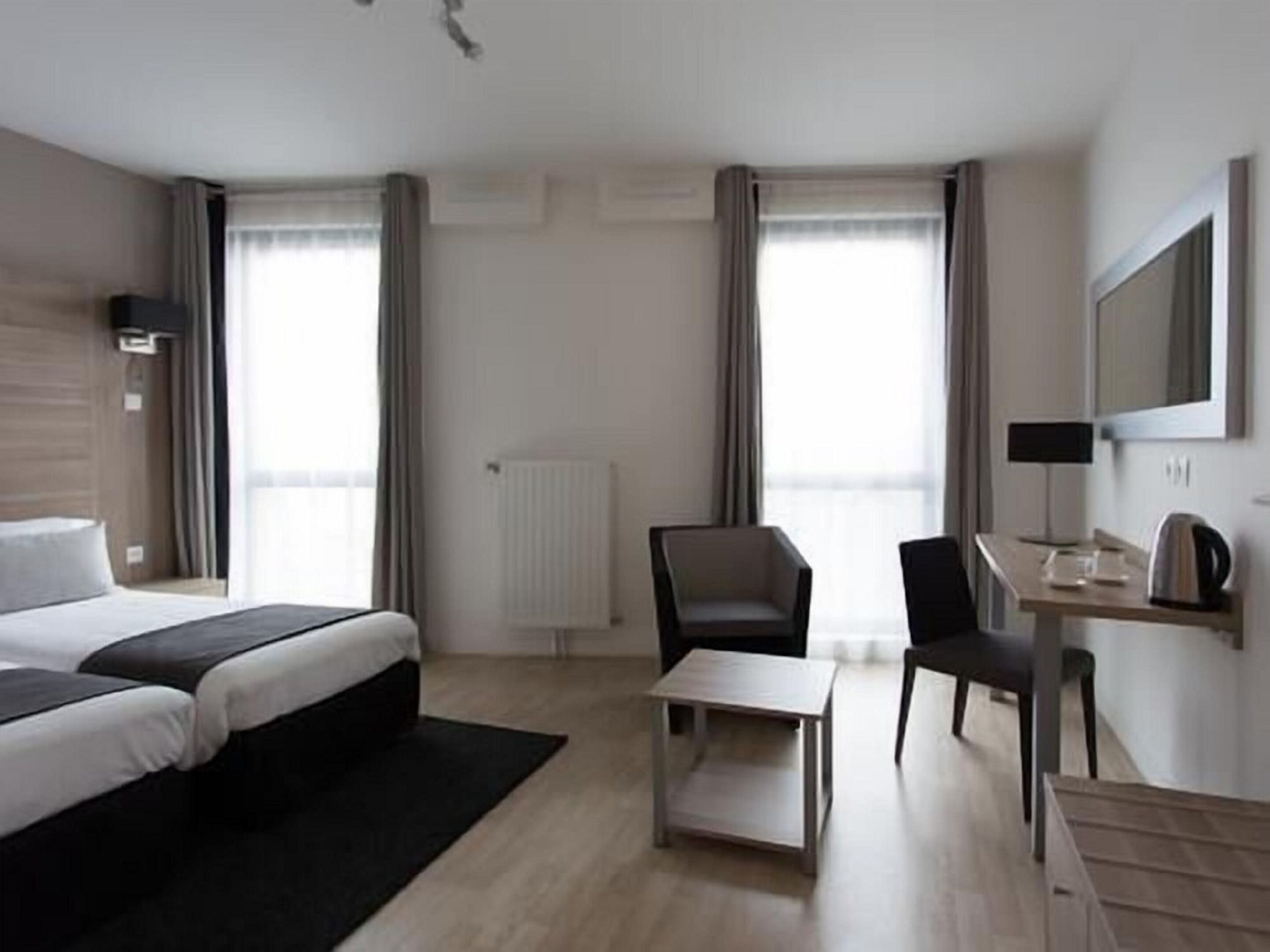 Une chambre d’hôtel avec un lit, un bureau, une chaise, un radiateur et une fenêtre avec des rideaux.