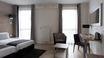 Une chambre d’hôtel avec un lit, un bureau, une chaise, un radiateur et une fenêtre avec des rideaux.