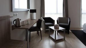 Ett hotellrum med ett skrivbord i trä, två stolar, ett litet bord, en spegel och en säng.