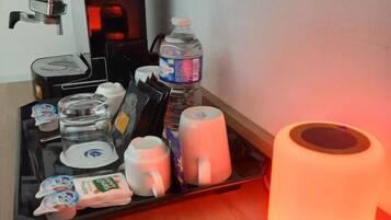 A coffee station with a coffee machine, water bottle, mugs, and tea bags.