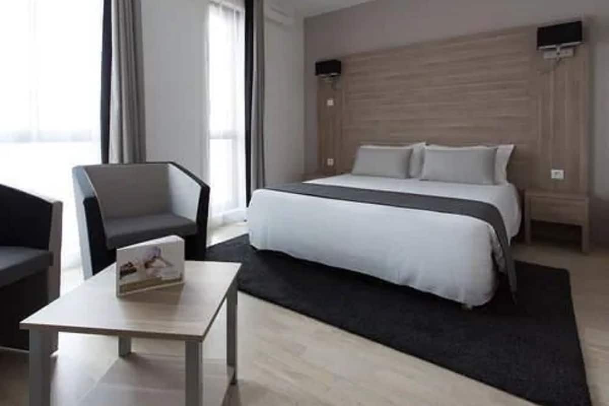 A modern hotel room with a bed, a small table, a chair, and a nightstand.