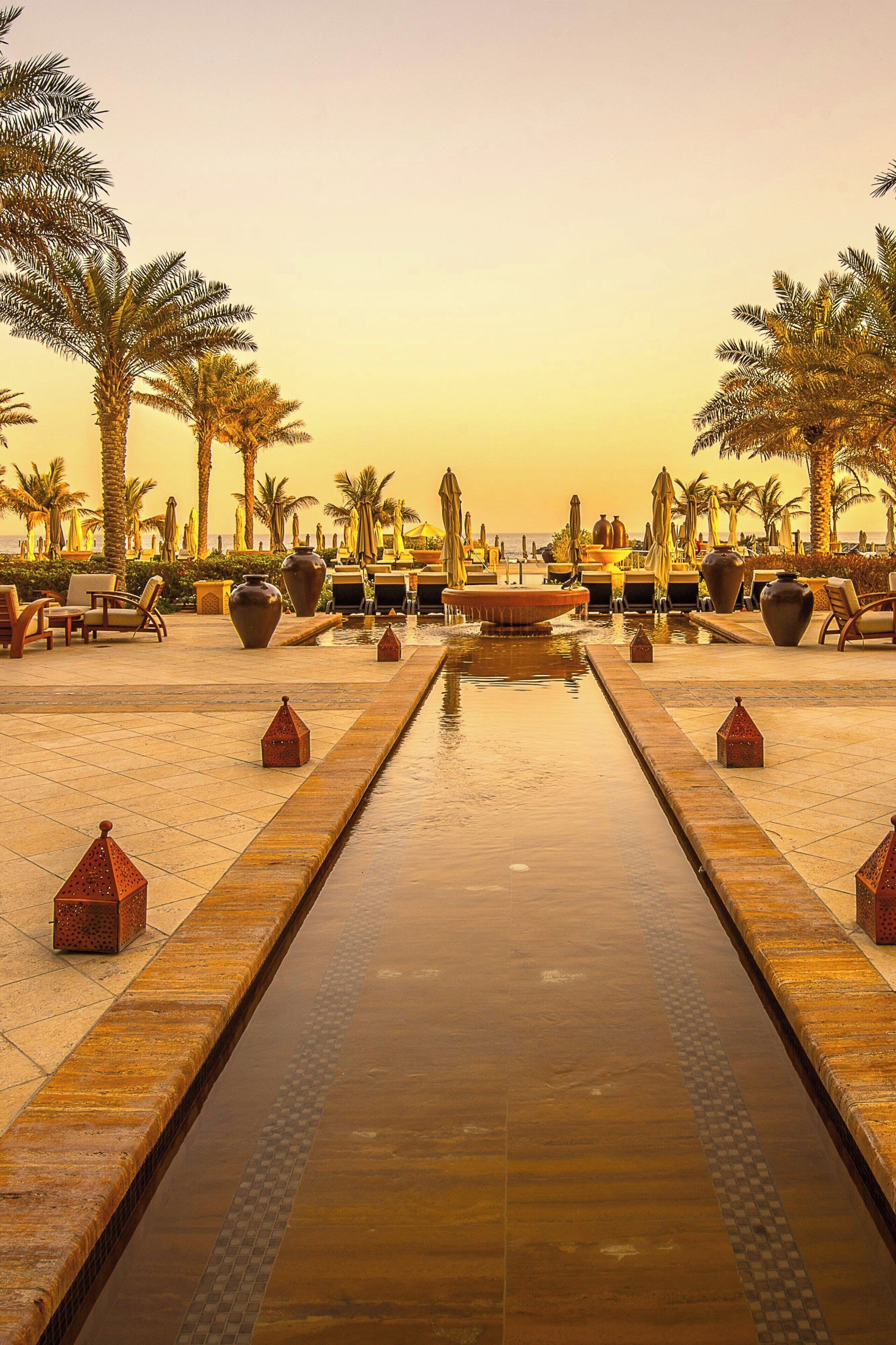 A pool area with palm trees, lounge chairs, and a water feature.