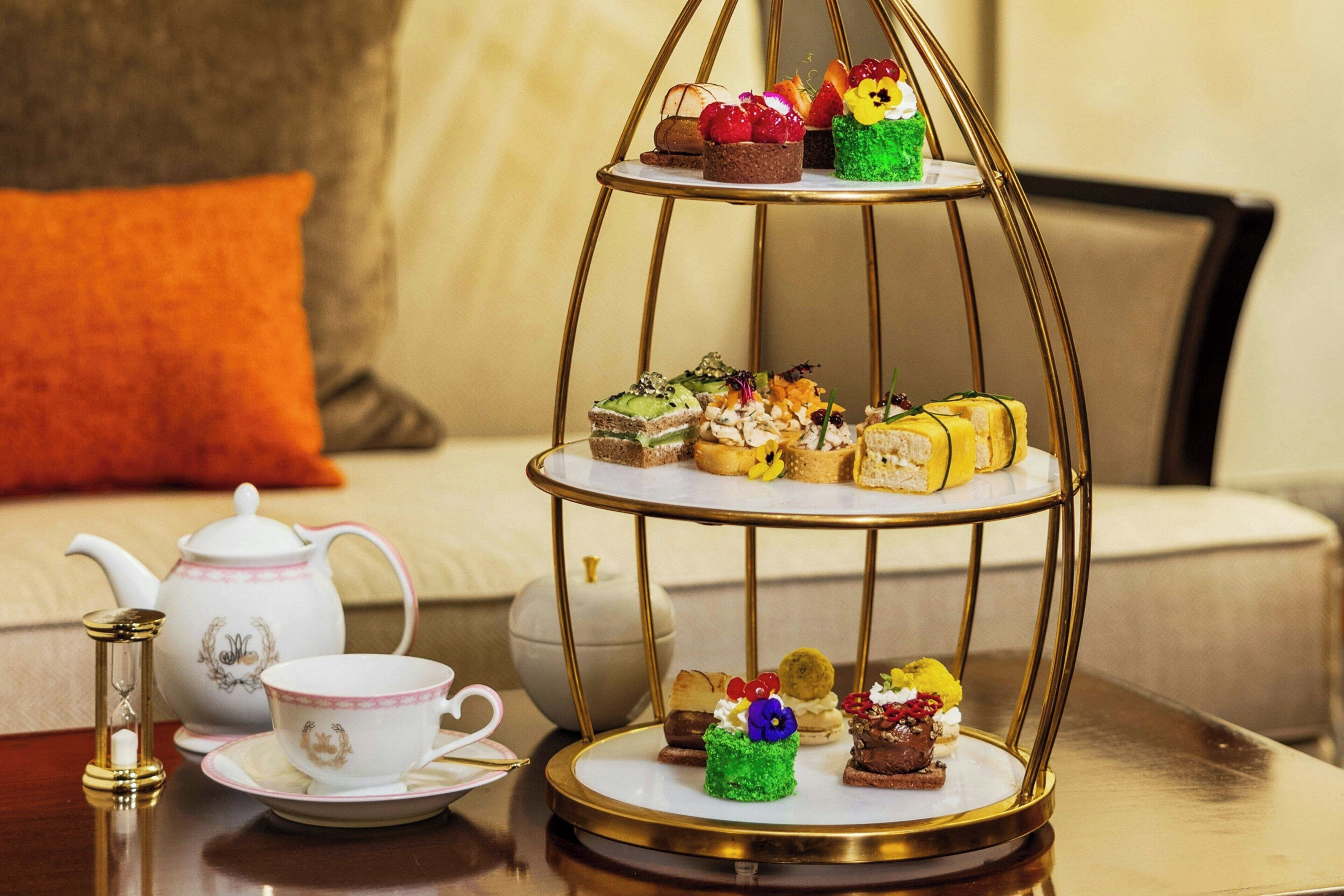 Un présentoir à trois niveaux, garni de diverses pâtisseries, et un service à thé disposés sur une table.