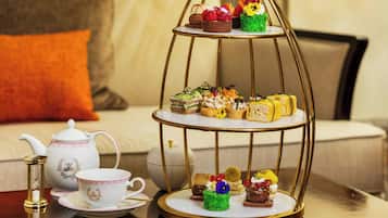 Un présentoir à trois niveaux, garni de diverses pâtisseries, et un service à thé disposés sur une table.
