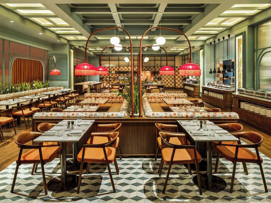 A spacious restaurant with multiple dining areas, each featuring wooden tables and orange chairs.