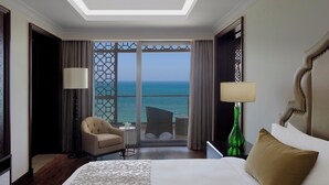 A hotel room with a large bed, a chair, a small table, and a view of the ocean through a glass door. - Ajman Saray, a Luxury Collection Resort, Ajman (Ajman)