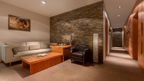 A modern living room with a stone wall, a sofa, a coffee table, a leather chair, and a wooden side table. - Ramada Resort by Wyndham Kranjska Gora (Kranjska Gora)