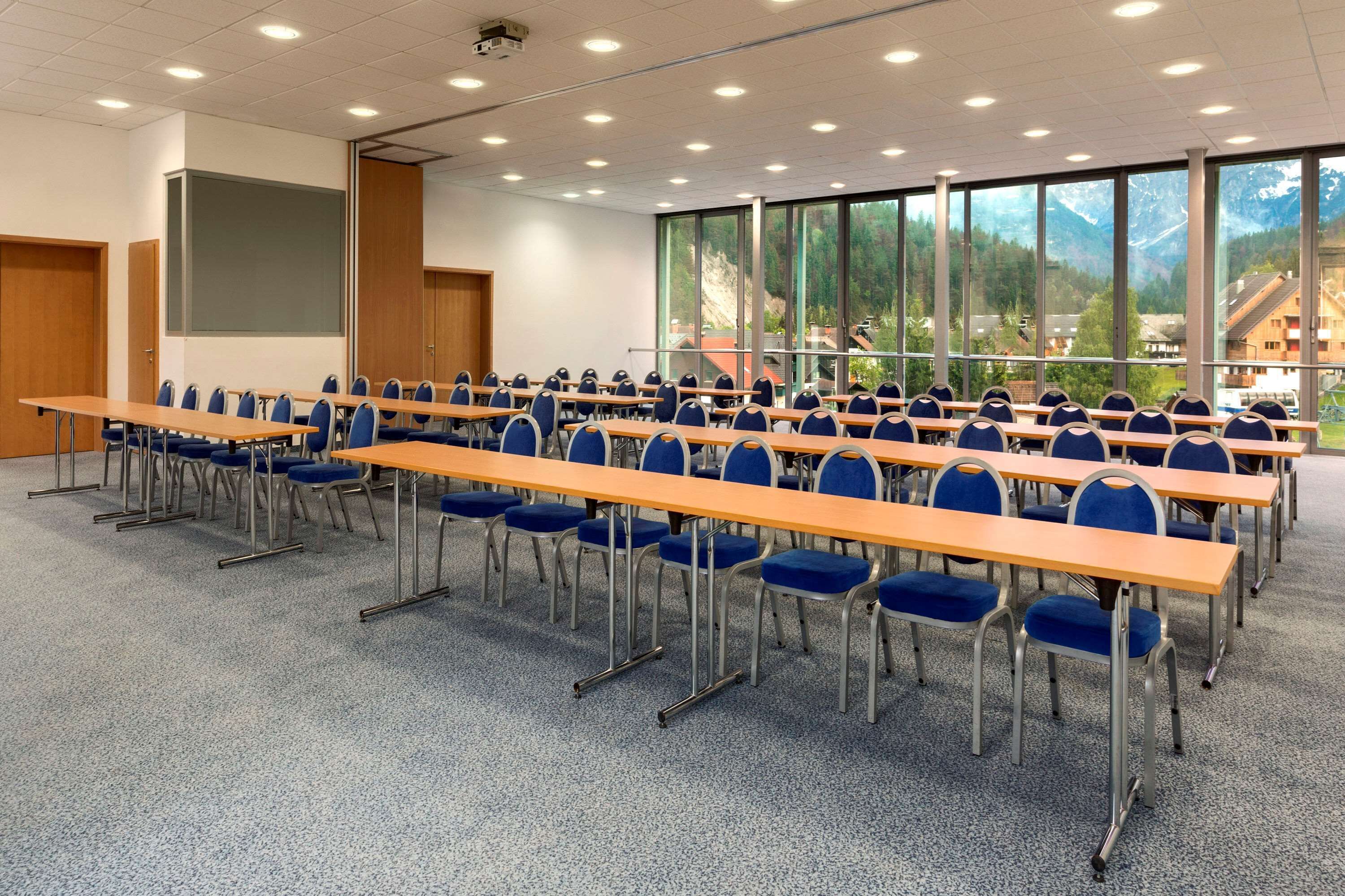 A conference room with rows of tables and chairs, large windows with a mountain view, and a projector screen.