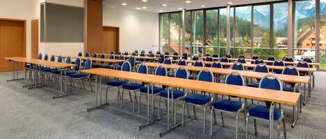 A conference room with rows of tables and chairs, large windows with a mountain view, and a projector screen.