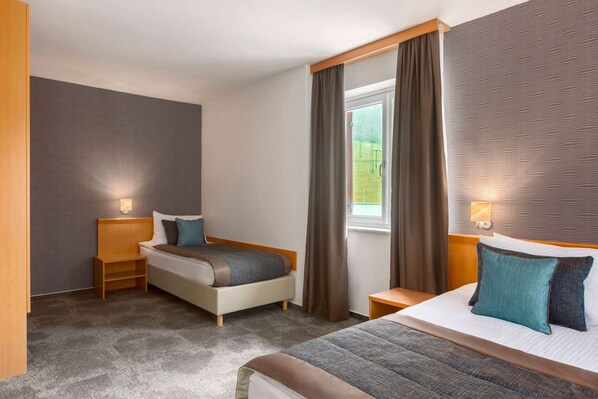 Una habitación de hotel con cama, mesita de noche, cortinas en la ventana y una lámpara de pared.
