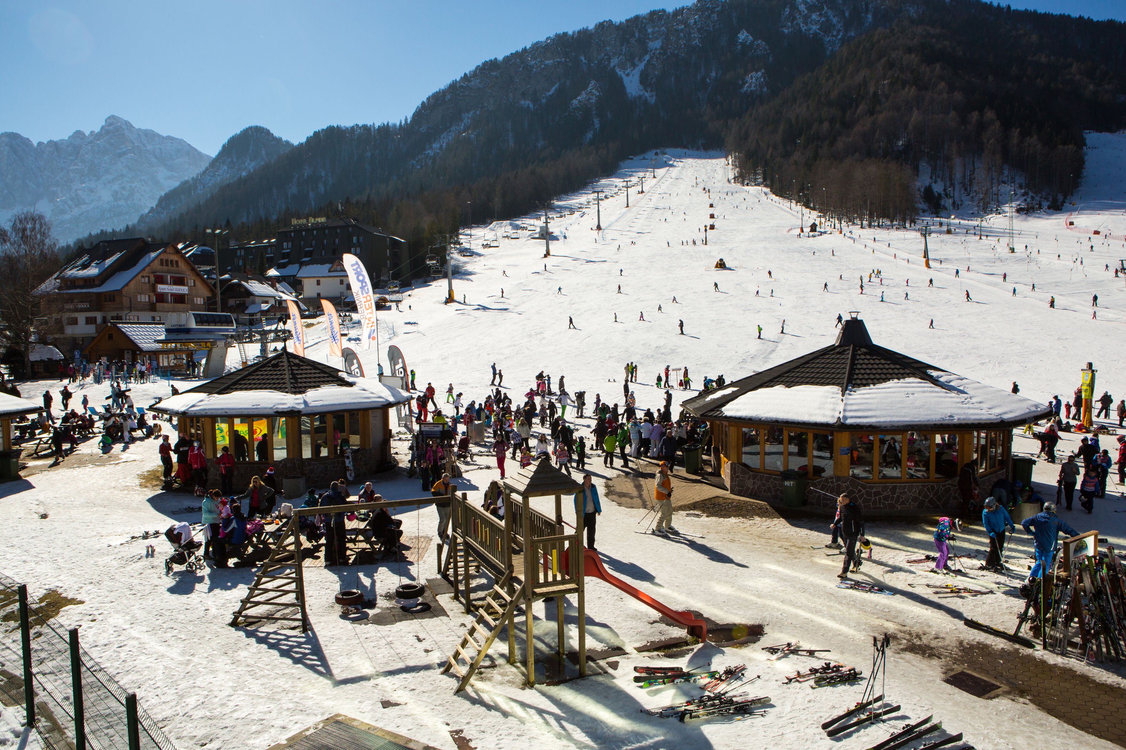 Una stazione sciistica con un'area giochi, noleggio sci e una pista da sci ampia.