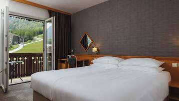 Ein Hotelzimmer mit einem großen Bett, einem Schreibtisch, einem Stuhl und einem Balkon mit Blick auf eine grüne Landschaft und ein Gebäude.