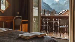 A hotel room with a bed, a desk, a chair, and a balcony with a view of mountains. - Ramada Resort by Wyndham Kranjska Gora (Kranjska Gora)