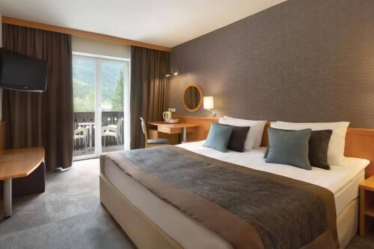 Een hotelkamer met een groot bed, een bureau, een stoel, een televisie en uitzicht op het omliggende landschap.