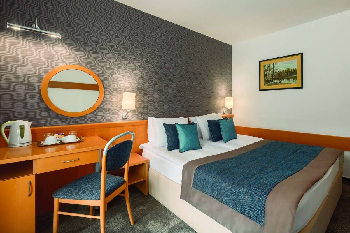 Een hotelkamer met een bed, een bureau met een stoel, een ronde spiegel en een schilderij aan de muur.