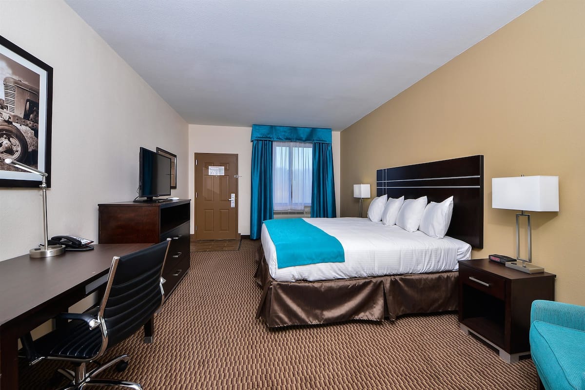 A hotel room with a bed, a desk, a chair, a TV, and a window with curtains.