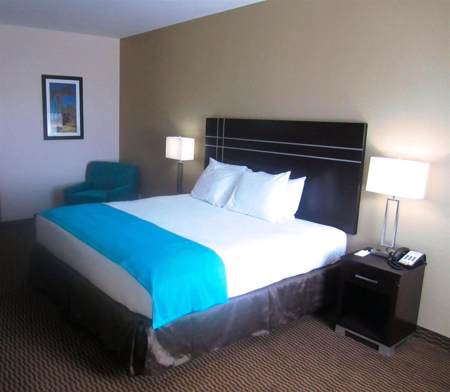 A hotel room with a large bed, two bedside lamps, a chair, and a small table with a phone.