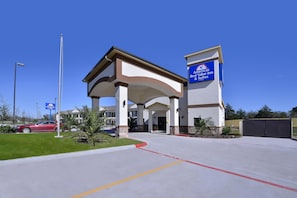 A hotel entrance with a clear sky, a red car parked outside, and a sign for 'America's Best Value Inn & Suites'. - Americas Best Value Inn & Suites Cuero (Cuero)