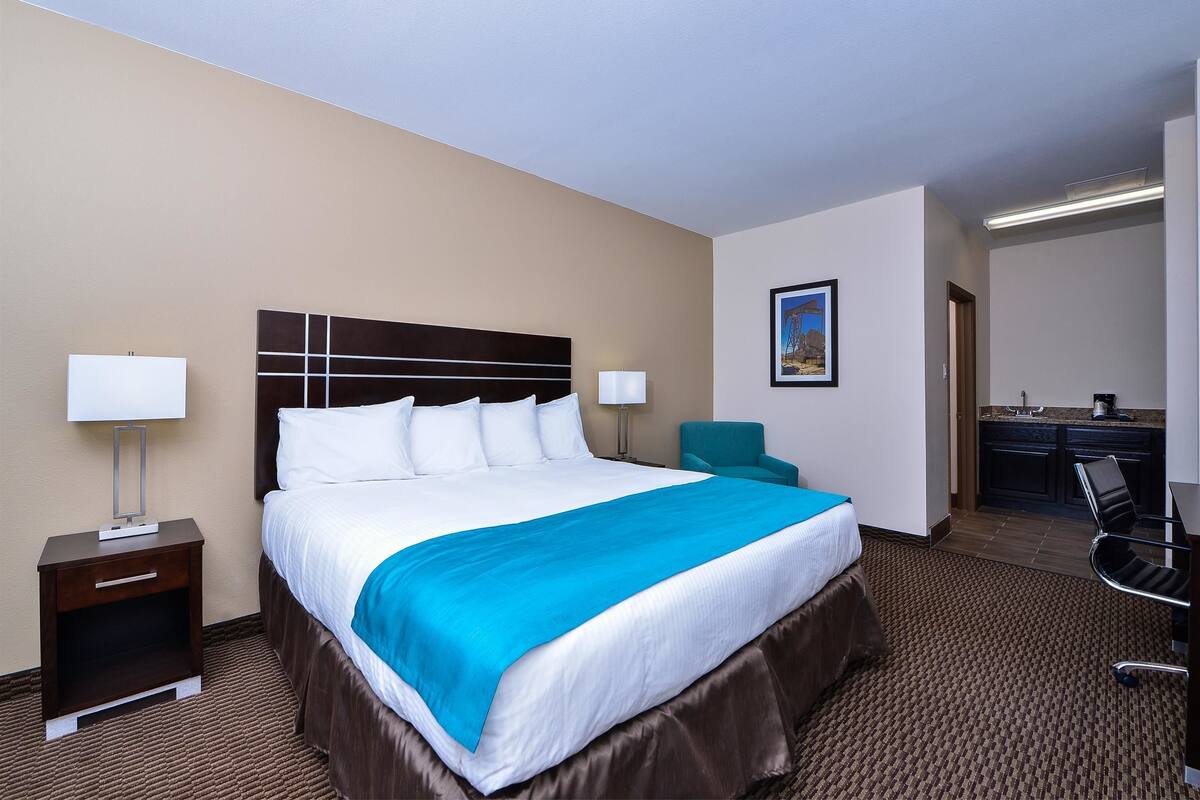 A hotel room with a large bed, a desk with a chair, a small table with a lamp, and a painting on the wall.