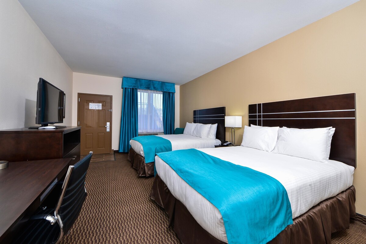 A hotel room with two beds, a desk, a television, and a door.