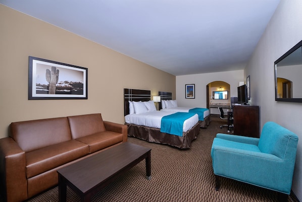 Een hotelkamer met een bruine leren bank, een turquoise fauteuil, een houten salontafel, een bed met witte lakens en een blauw accent, een flatscreen televisie, een bureau met stoel, en een ingelijst schilderij aan de muur.