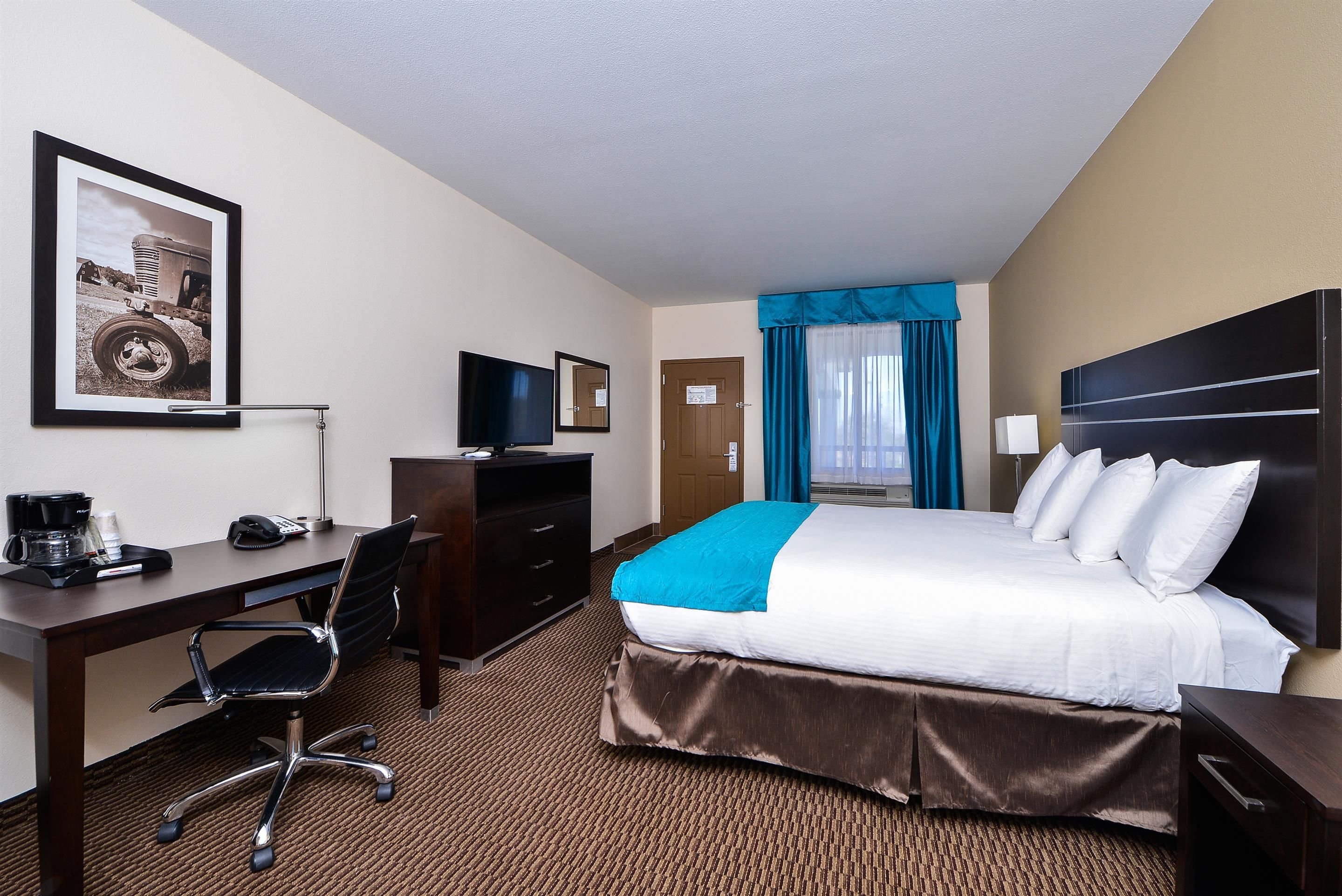 A hotel room with a bed, desk, chair, and a framed picture on the wall.