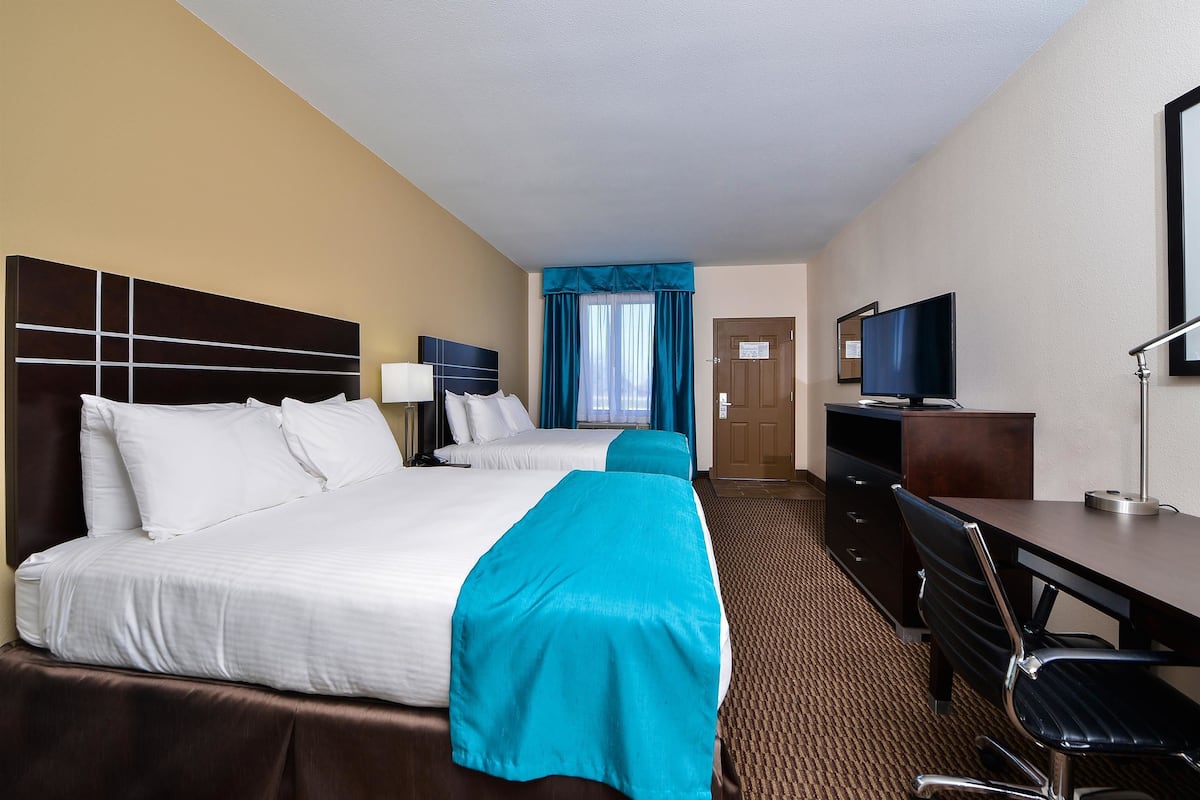 A hotel room with two beds, a desk, a chair, a television, and a door.