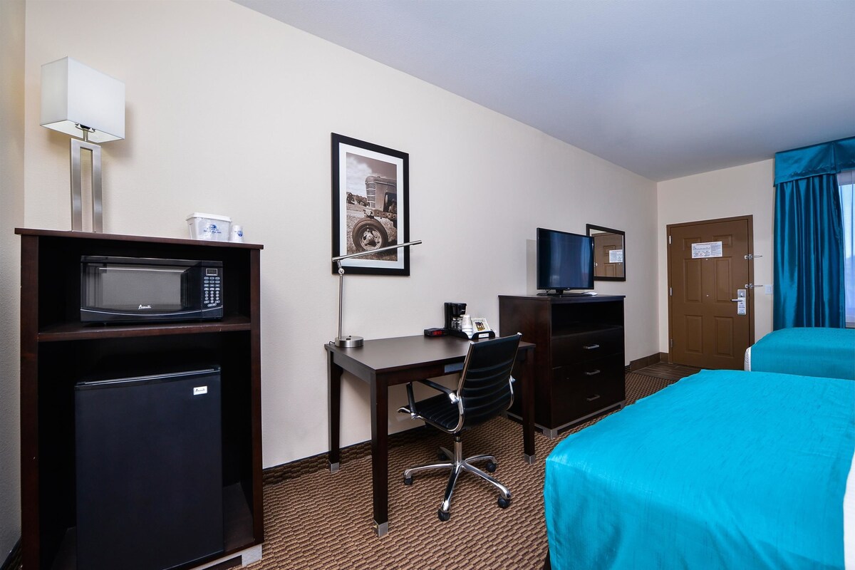A hotel room with a desk, a microwave, a refrigerator, a chair, a bed, a television, and a door.