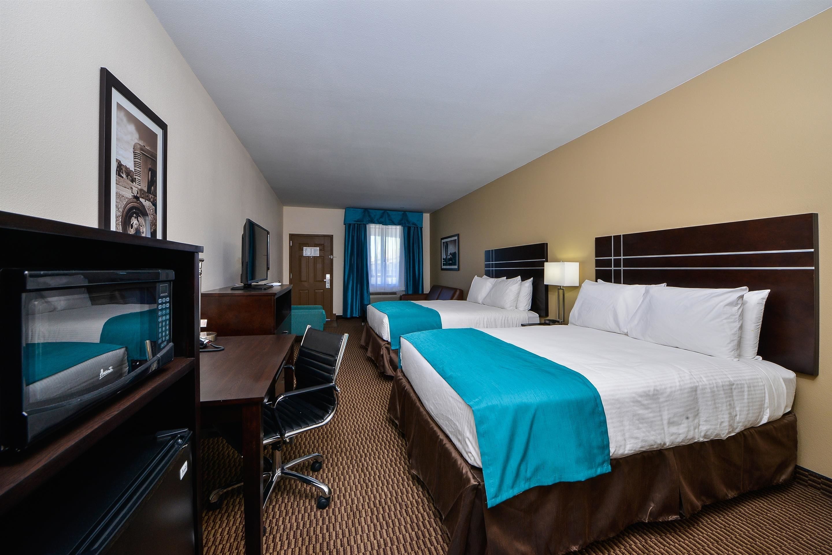 A hotel room with two beds, a desk with a chair, a television, and a bathroom visible through an open door.
